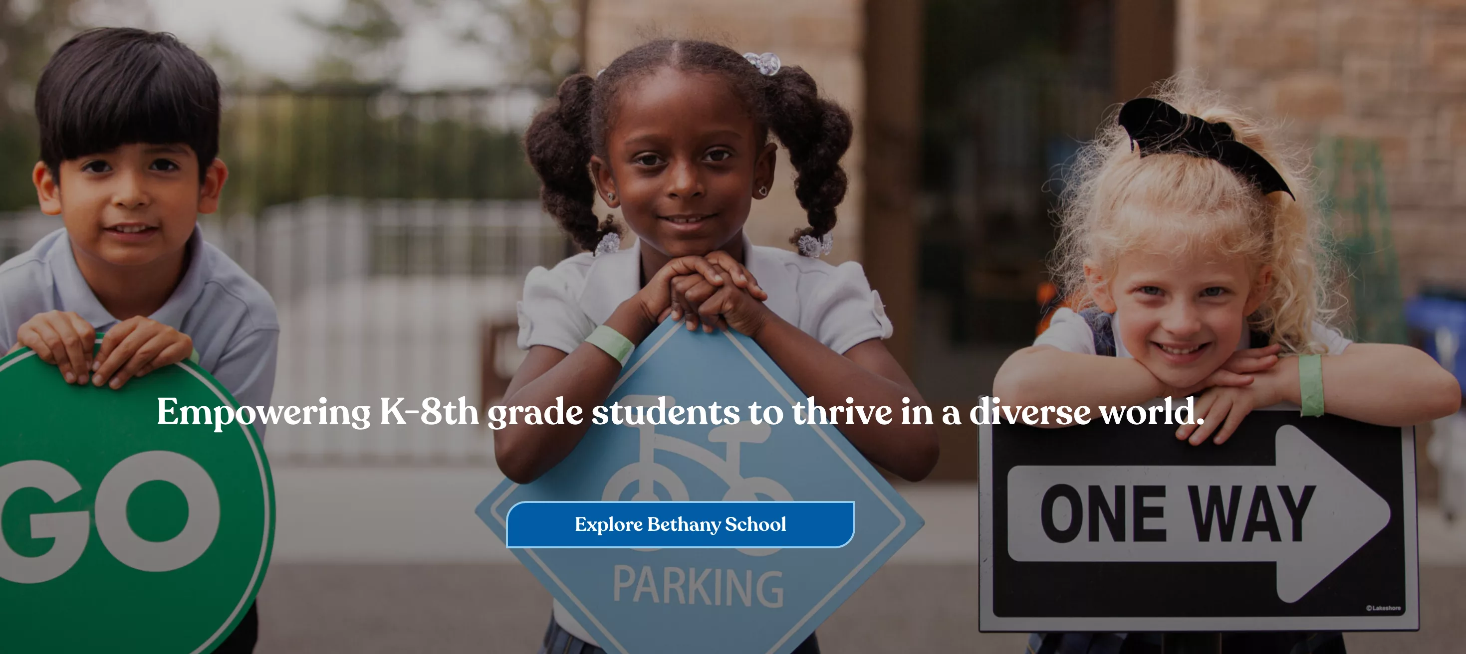 Three diverse K-8 students holding signs and smiling, representing empowerment and inclusivity.