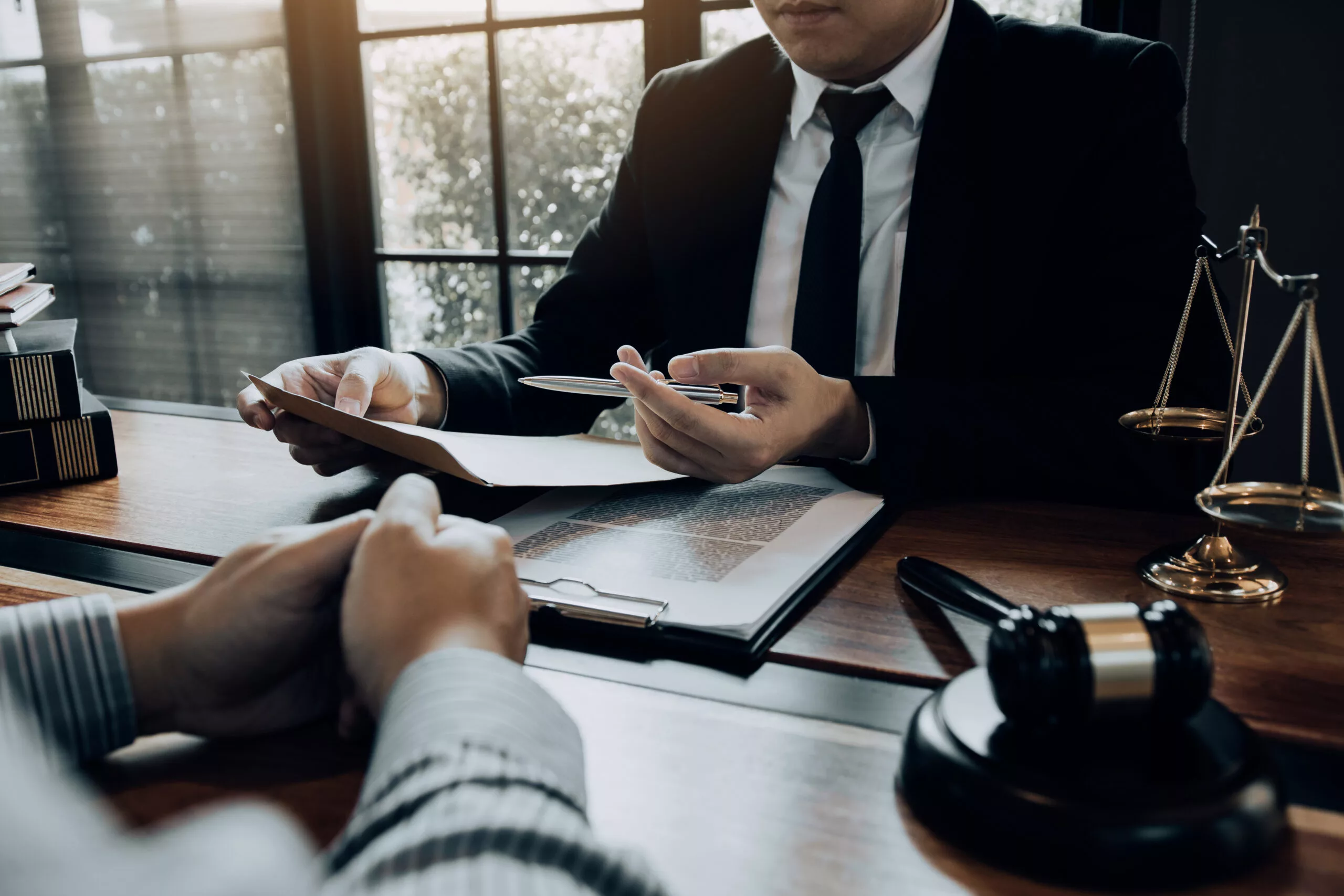 Lawyer consulting with a client, discussing legal documents in an office with scales of justice on the desk.